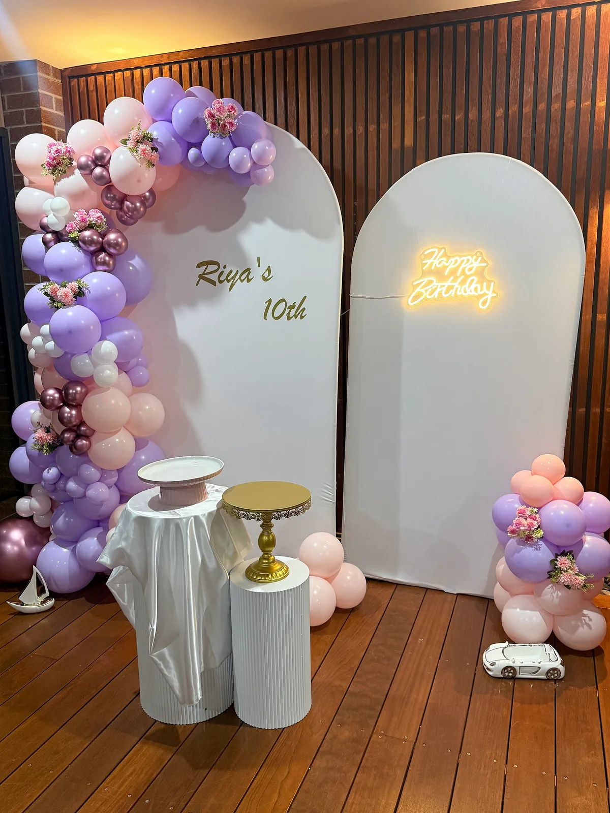 Pink and lilac 10th birthday setup in Aintree with personalised white arches, floral balloon garland, birthday light and cake plinths.